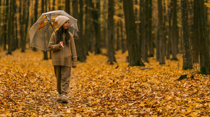 Young girl with umbrella walking through a beautiful autumn forest