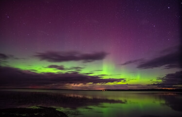 Vivid green and purple aurora borealis lights dance above a calm lake with stars and reflections on a tranquil night