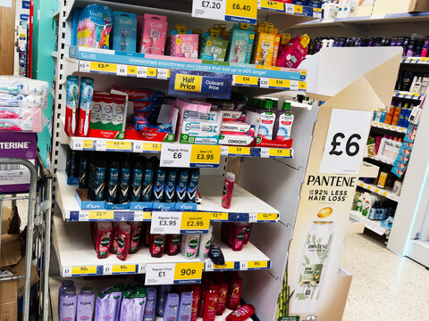 Shoppers in a Manchester Tesco pharmacy aisle compare toothpaste and hair care products on shelves