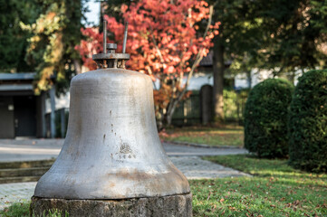Abgehängte Kirchenglocke mit Jahreszahl 1949 auf Steinsockel vor Baum mit Herbstlaub und Hecke beim Friedhof in Reutlingen-Mittelstadt