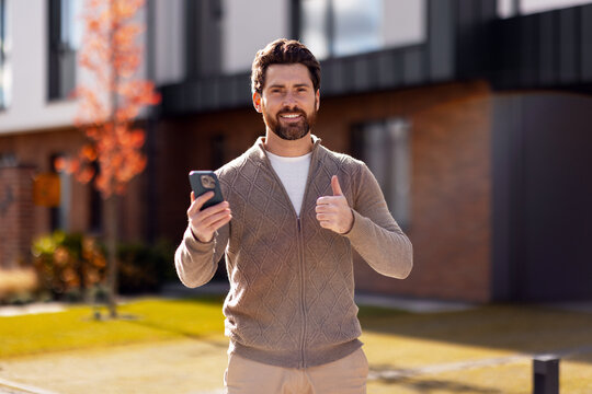 Happy man holding phone giving thumbs up outdoors