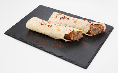 Two crispy rolled Kebabs filled with seasoned beef rest on a dark slate board, lightly dusted with red chili powder