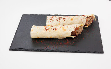 Two crispy rolled Kebabs filled with seasoned beef rest on a dark slate board, lightly dusted with red chili powder