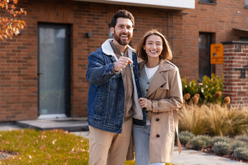 Happy couple holding house keys standing in front of new home