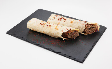 Two crispy rolled Kebabs filled with seasoned beef rest on a dark slate board, lightly dusted with red chili powder
