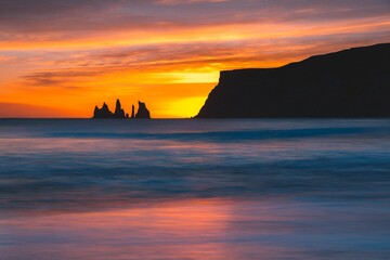 Calm mountain silhouette, water waves and black sand beach. Reynisdrangar sea stacks at cold winter during sunset in Iceland. Beautiful nature landscape background for wallpaper