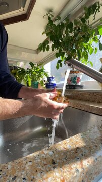 Fregando, enjabonando y aclarando bajo el agua del grifo del fregadero en time lapse y tiempo acelerado con estropajo, esponja y jab&oacute;n lavavajillas en la cocina de casa con plantas
