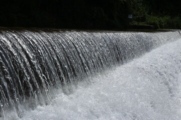 A close-up of water cascading over a small weir or dam, creating a thick sheet of sparkling white foam and spray.