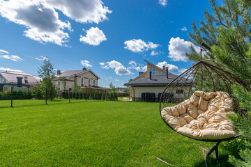 A spacious backyard with a green lawn and modern houses against a bright blue sky on a  sunny day. © Alhim