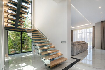 An elegant wooden staircase with glass railings leads to a spacious living room filled with natural...