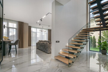 A modern living space with an elegant staircase and an open floor plan providing natural light during the daytime.