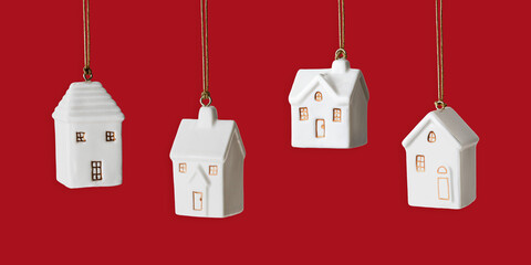 Set of White ceramic houses ornament hanging, festive red banner. Side view New Year cute toys. Concept of real estate, mortgage, new home, family comfort and holiday mood, minimal seasonal designs