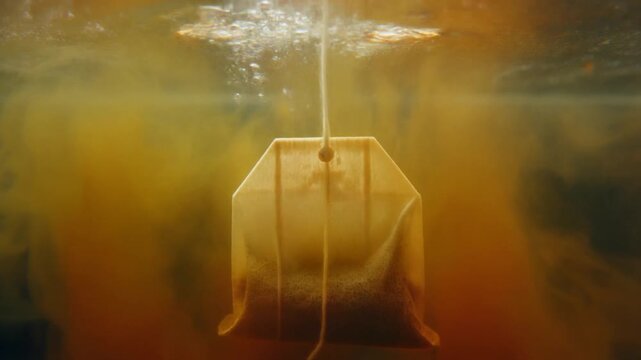 Tea bag dipping into clear water, with the color blooming beautifully like watercolor art and subtle reflections or flashbacks appearing in the liquid