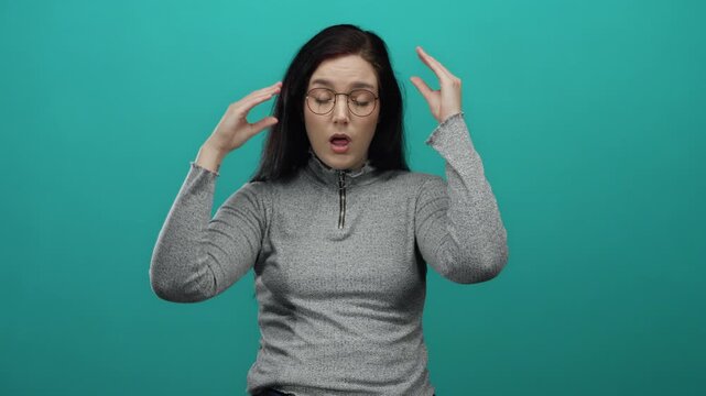 Woman wearing glasses gesturing thoughtfully against a green background, showcasing a casual and contemplative expression with her eyes closed and hands near her face.