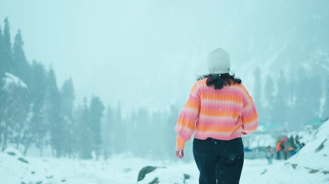 4K back view of young woman walking in mountain landscape at Gulmarg, Jammu and Kashmir, India .White snowy blanket on mountains and trees. Beauty of winter wonderland. Concept of adventure and travel