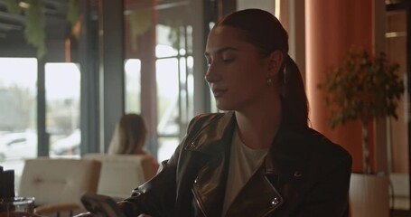 A focused young businesswoman in a modern cafe, actively using her smartphone for digital communication. She takes a refreshing break, showcasing a productive and connected urban lifestyle. - Powered by Adobe