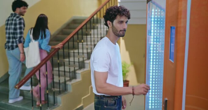 Indian happy young adult gen z smart male man use easy fast self service choose juice drink press button campus area. Lady female walk stairway thirsty boy take bottle enjoy break day time hall way