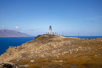 scenic landscape with rocky cliff and old whitewashed lighthouse on deep blue aegean sea background. Armenistis Lighthouse, Mykonos, Greece 