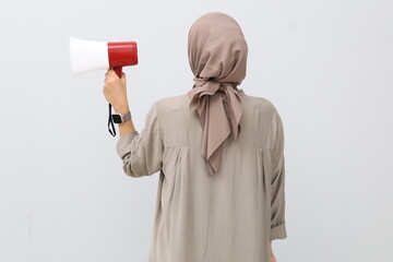 Back view of young Asian woman in hijab holding megaphone, isolated on white background, speech and announcement concept.