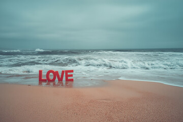 Red "LOVE" Word Sign on a Serene Sandy Beach with Ocean Waves - Romance and Valentine's Day Concept