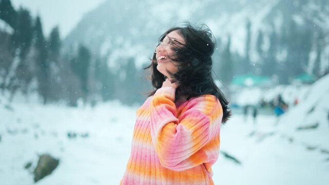 4K Portrait of happy Indian woman standing under snowfall in mountains at Pahalgam, Kashmir, India. Young woman winter portrait. Close-up portrait of happy girl. Tourist enjoying holidays.