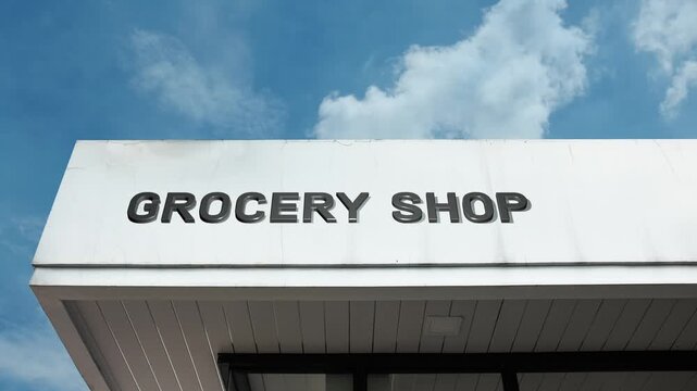 Grocery Shop word sign clearly displayed on the commercial retail building facade beneath a clear blue sky, signifying a neighborhood store specializing in selling a general range of food and supplies