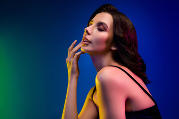 Fototapeta premium Stylish sensual brunette woman posing in neon lighting with vibrant makeup in an elegant dress showcasing beauty