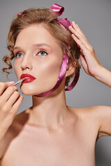 Obraz premium Curly-haired woman applies red lipstick, showcasing beauty with pink ribbon charm