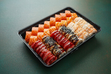 sushi rolls assortment with salmon tuna shrimp eel in black tray on green background