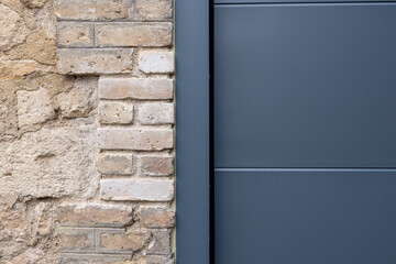 Porte de garage grise anthracite installée par un professionnel, encadrée par un mur en pierre beige et un sol en macadam, entre modernité et authenticité.