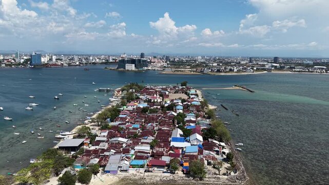 Aerial view of Lae-Lae Island near Makassar, Indonesia, showing colorful coastal houses surrounded by turquoise sea and city skyline in the background.	