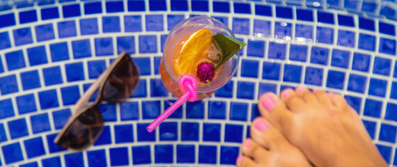 A woman in the pool drinks a cocktail. Selective focus.