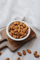 Bowl of organic almonds on wooden board, healthy snack ingredients, natural food spread