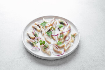 Marinated herring slices with red onion and herbs on white plate over light background