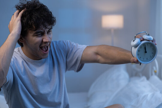 Shocked man waking up late and looking at alarm clock with frustration. Early morning bedroom scene reflects oversleeping, stress, and time management issues in daily life.