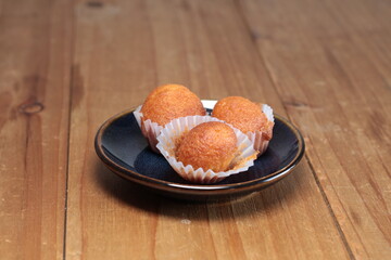 Golden baked mini muffins in paper cups presented on a dark plate, resting on a textured wooden table