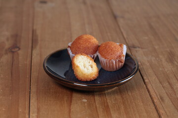 Golden baked madeleine cakes with one open, showcasing fluffy texture on a dark plate over a rustic wooden surface