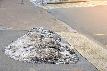 Melting dirty snow pile beside city crosswalk after municipal snow removal showing winter cleanup and icy pedestrian hazard on urban street, leftover slushy snow residue near tactile pavement