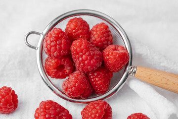 Raspberries in strainer with scattered berries for snack prep or summer dessert concept