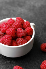 Raspberries in cup on black textured background for gourmet snack or modern food styling concept