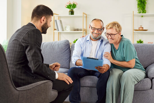 Smiling elderly couple meets agent at home, reviewing documents and signing agreements while discussing real estate options. Seniors discussing insurance or investment contract with advisor