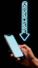 Neon "Order Here" vertical arrow points to hand holding smartphone on black background