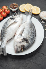 Fresh raw dorado fish on white plate with lemon tomatoes and spices