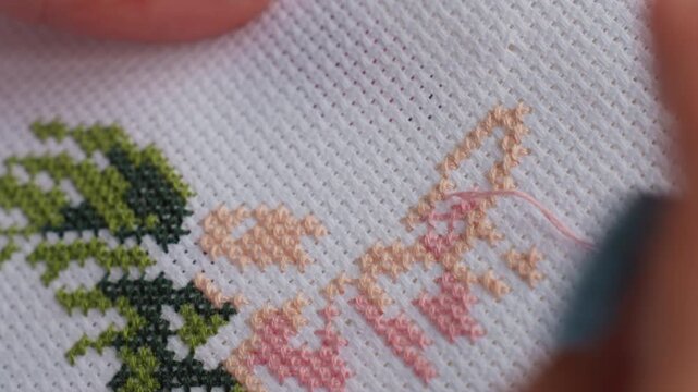 Extreme close up skilled person embroidering fabric tree like design using fine needlework, blue painted nails guiding thread through textured cloth creating detailed pattern with artistic precision
