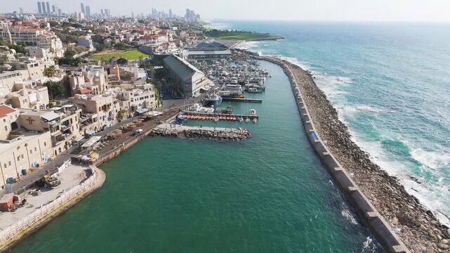 Aerial view of the turquoise sea meeting the historic Old Jaffa port, contrasting with the beige buildings, Tel Aviv-Yafo, Israel.