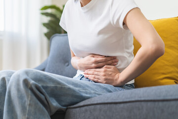 Sick asian young woman in pain, hand holding belly, stomach pain from food poisoning, girl hurt...