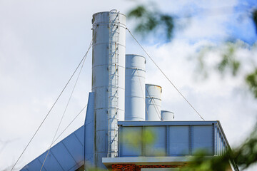 Industrial building with tall metal chimneys and support cables against a cloudy sky, representing manufacturing, engineering, and modern industrial architecture in an urban environment