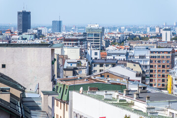 Fototapeta premium Expansive cityscape of Belgrade, Serbia, capturing a blend of old and modern architecture with green rooftops, apartment blocks, and tall business towers rising across the bright horizon .