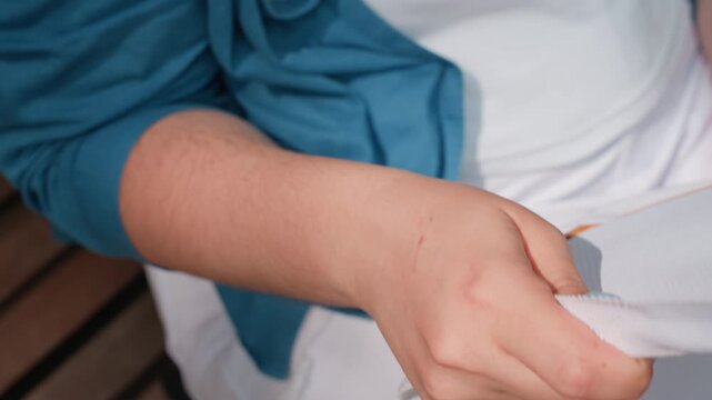 close up woman fanning herself with fabric in warm sunlight, soft motion of hand, light blue nails visible, blue sleeve over white outfit, gesture expressing heat relief and relaxation