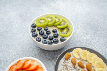 Three oatmeal bowls with kiwi banana and strawberry on gray background